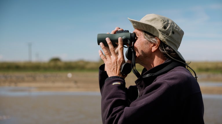 A man looking through binoculars at Sandilands nature reserve.